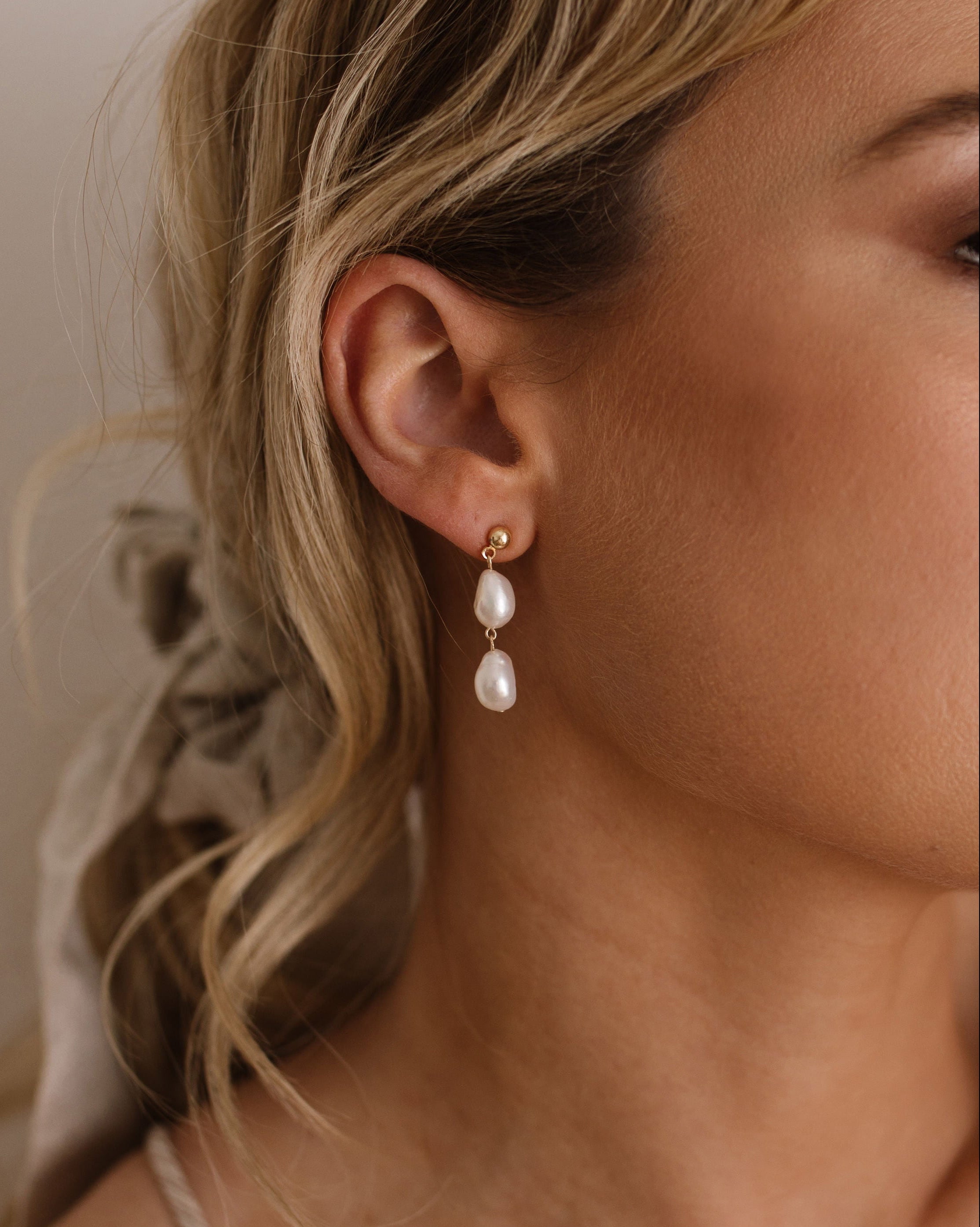Close-up of a woman wearing pearl earrings with a neutral background