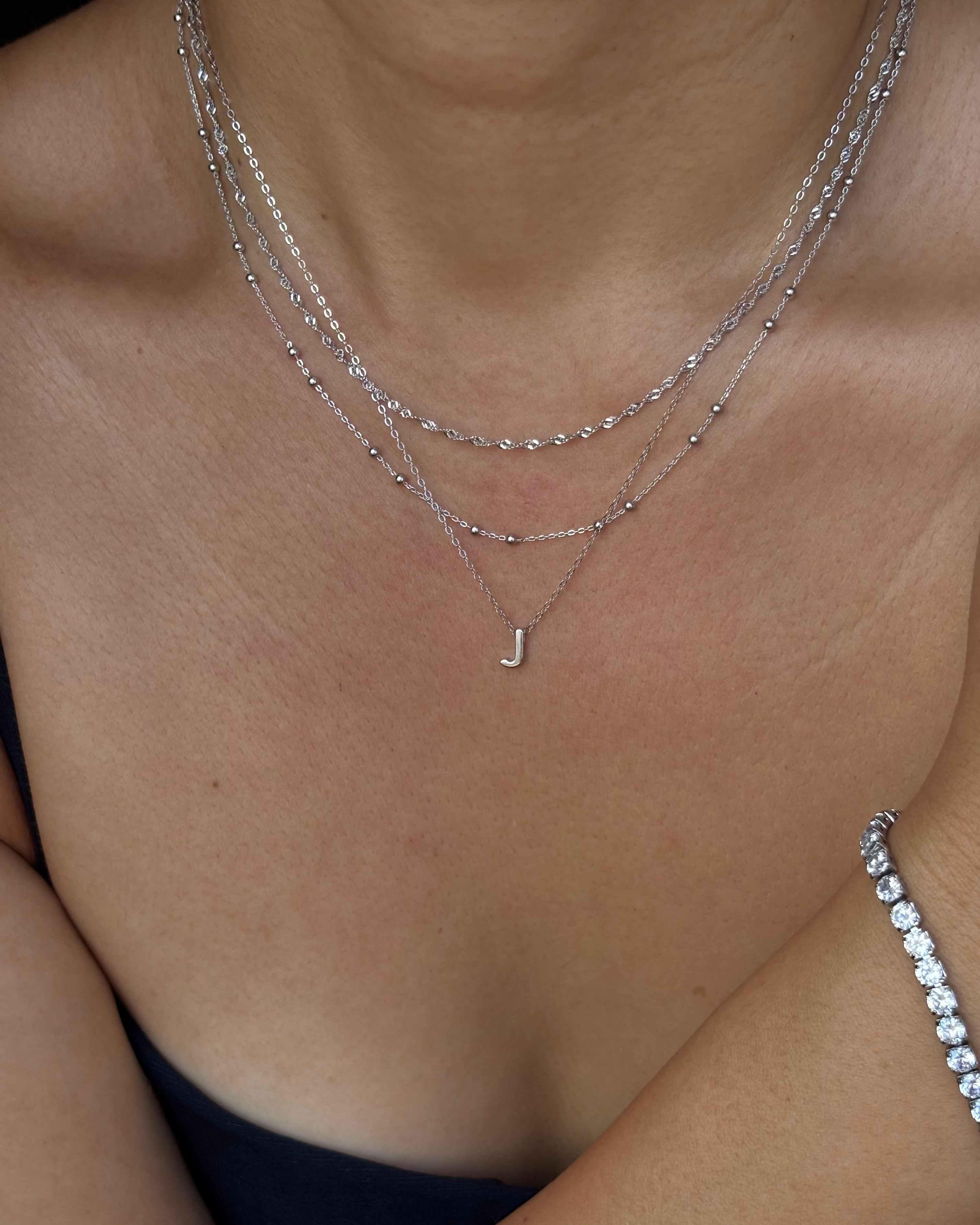 Close-up of a person wearing multiple necklaces with a 'J' pendant on a plain background