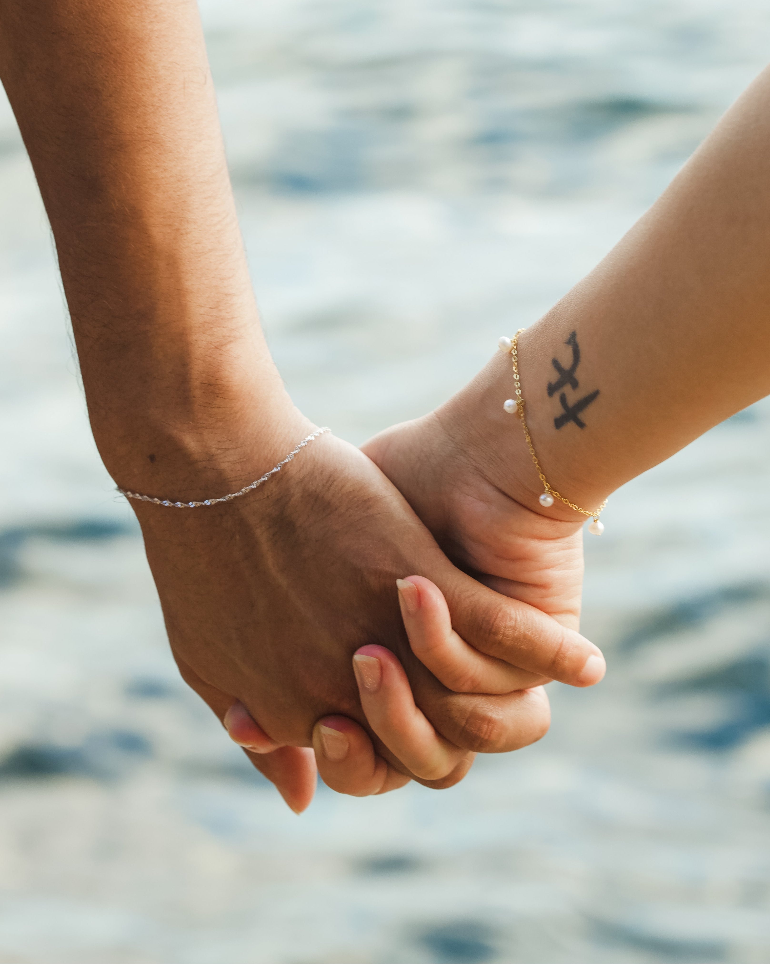 Two people holding hands with a blurred water background
