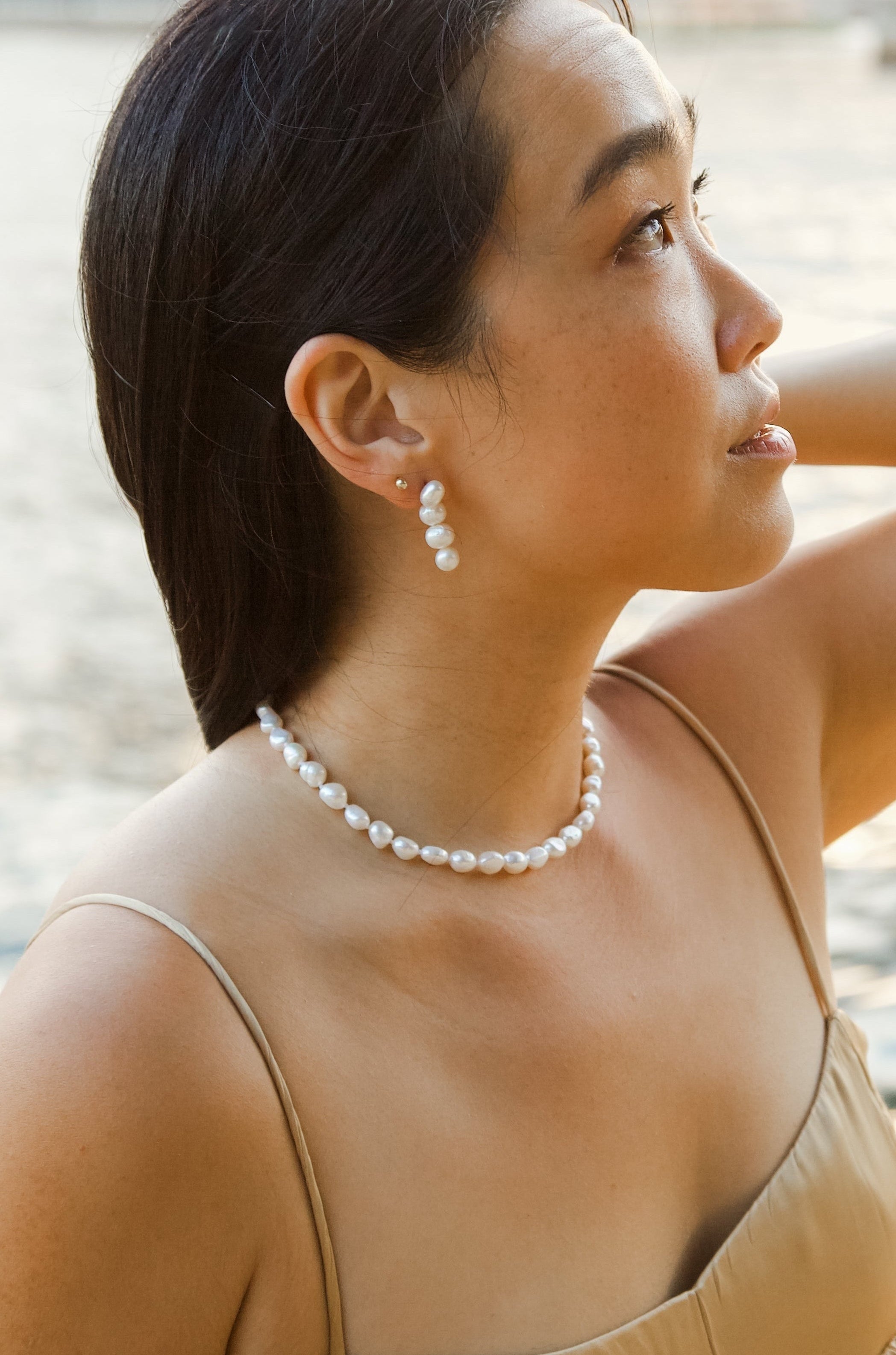 Woman in a beige dress with a pearl necklace by a waterfront