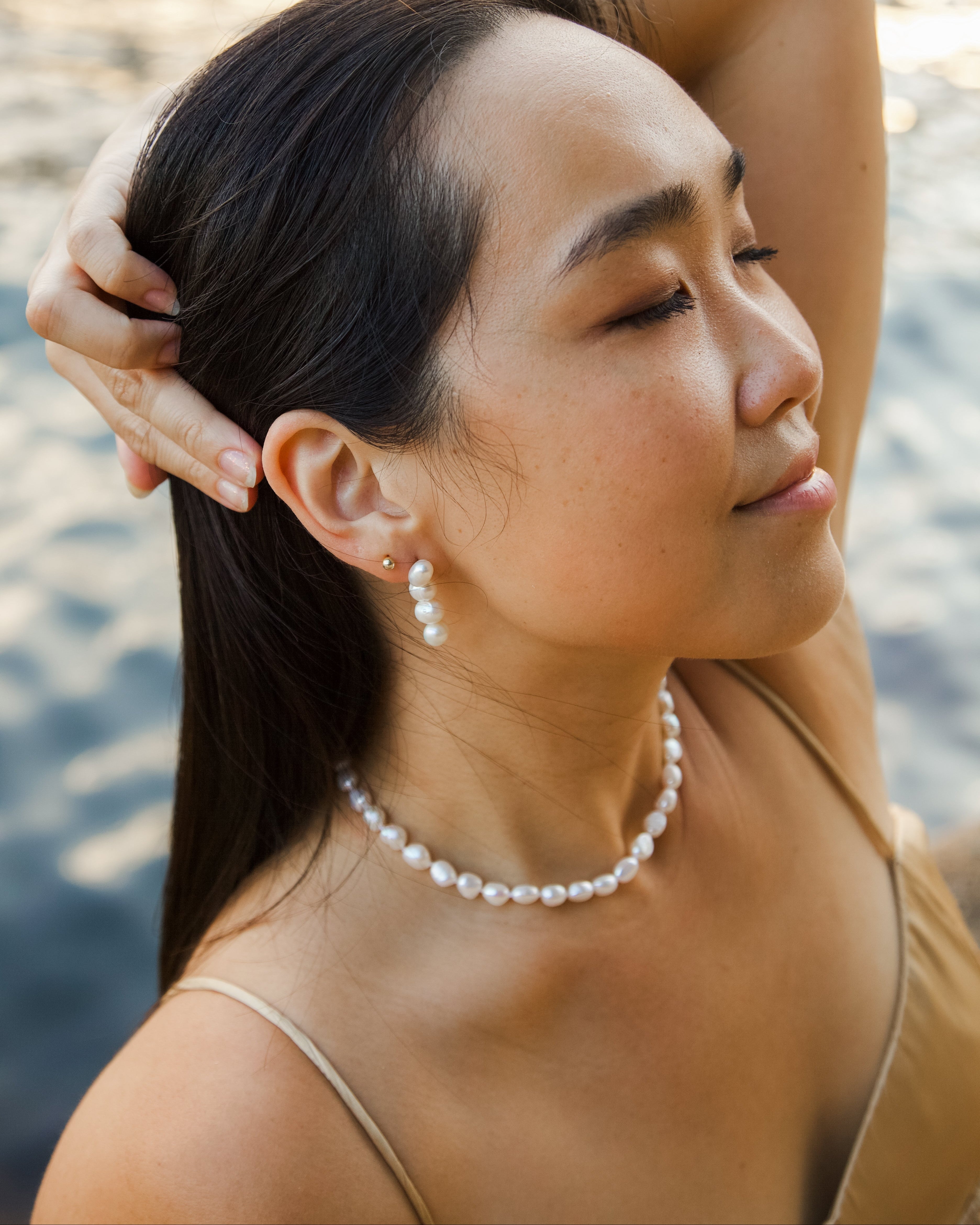 Woman with pearl necklace and earrings by a body of water