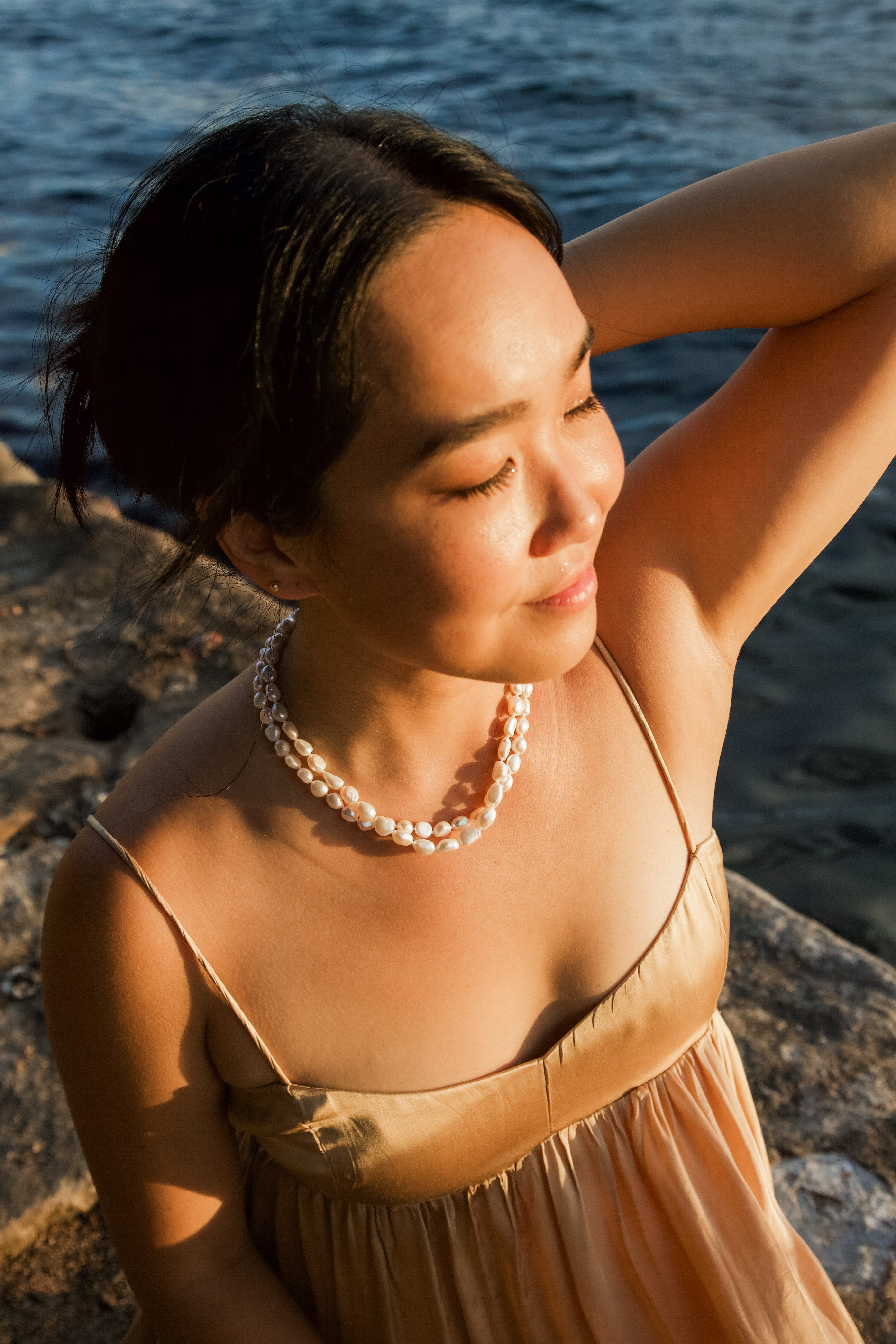 Woman in a beige dress with a pearl necklace by the water