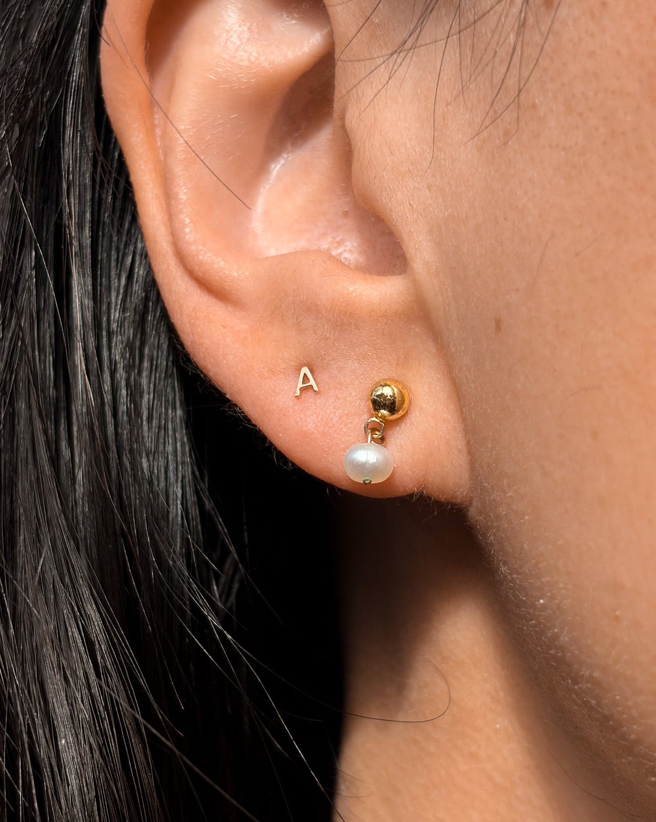 Close-up of an ear wearing gold and pearl stud earrings.