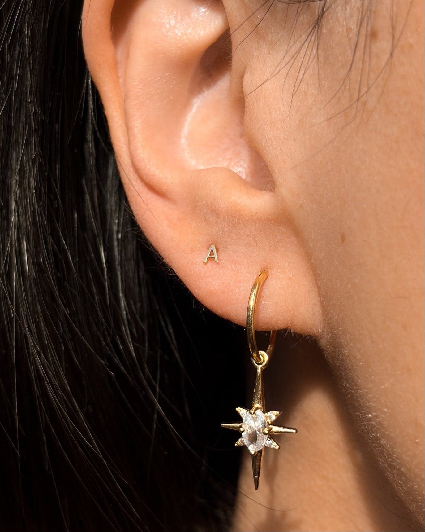 Close-up of an ear wearing a gold hoop earring with a star-shaped gemstone.