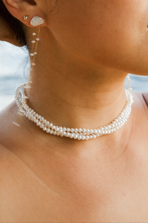Close-up of a person wearing pearl jewelry with a blurred natural background