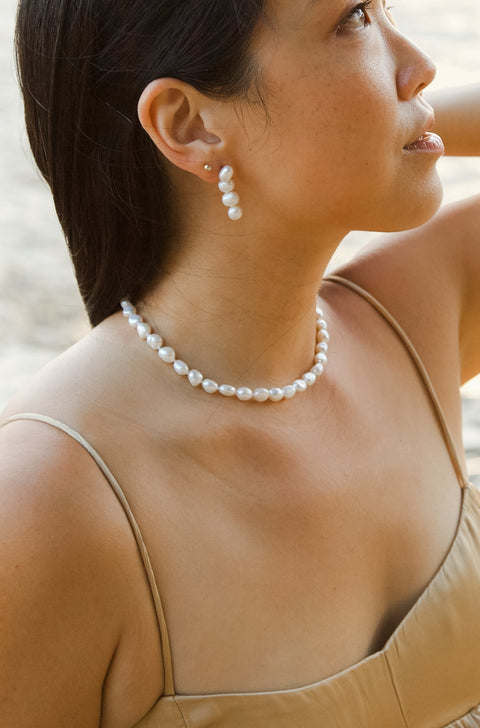 Woman in a beige dress with a pearl necklace by a waterfront