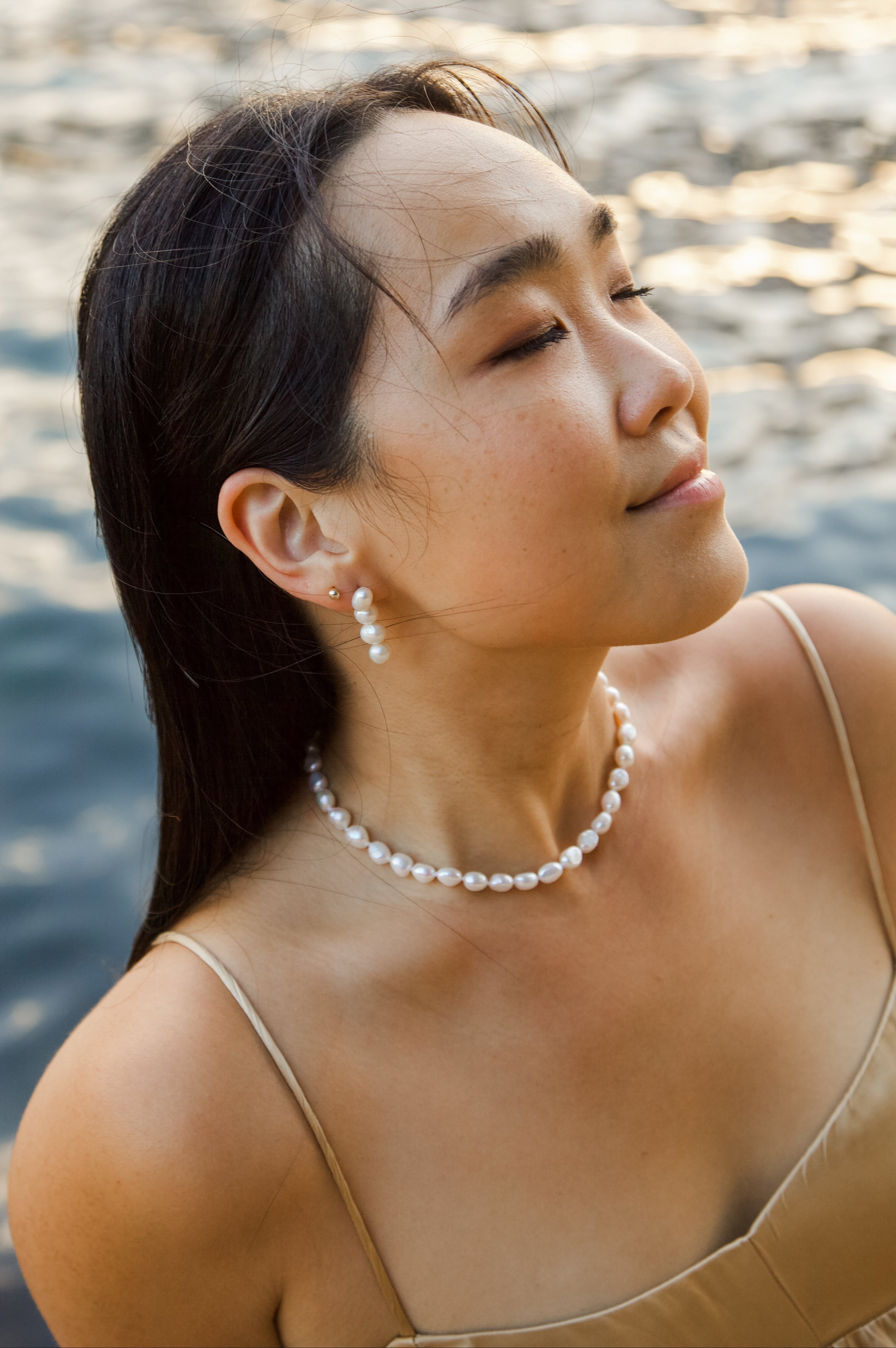 Woman wearing a pearl necklace and earrings by a body of water