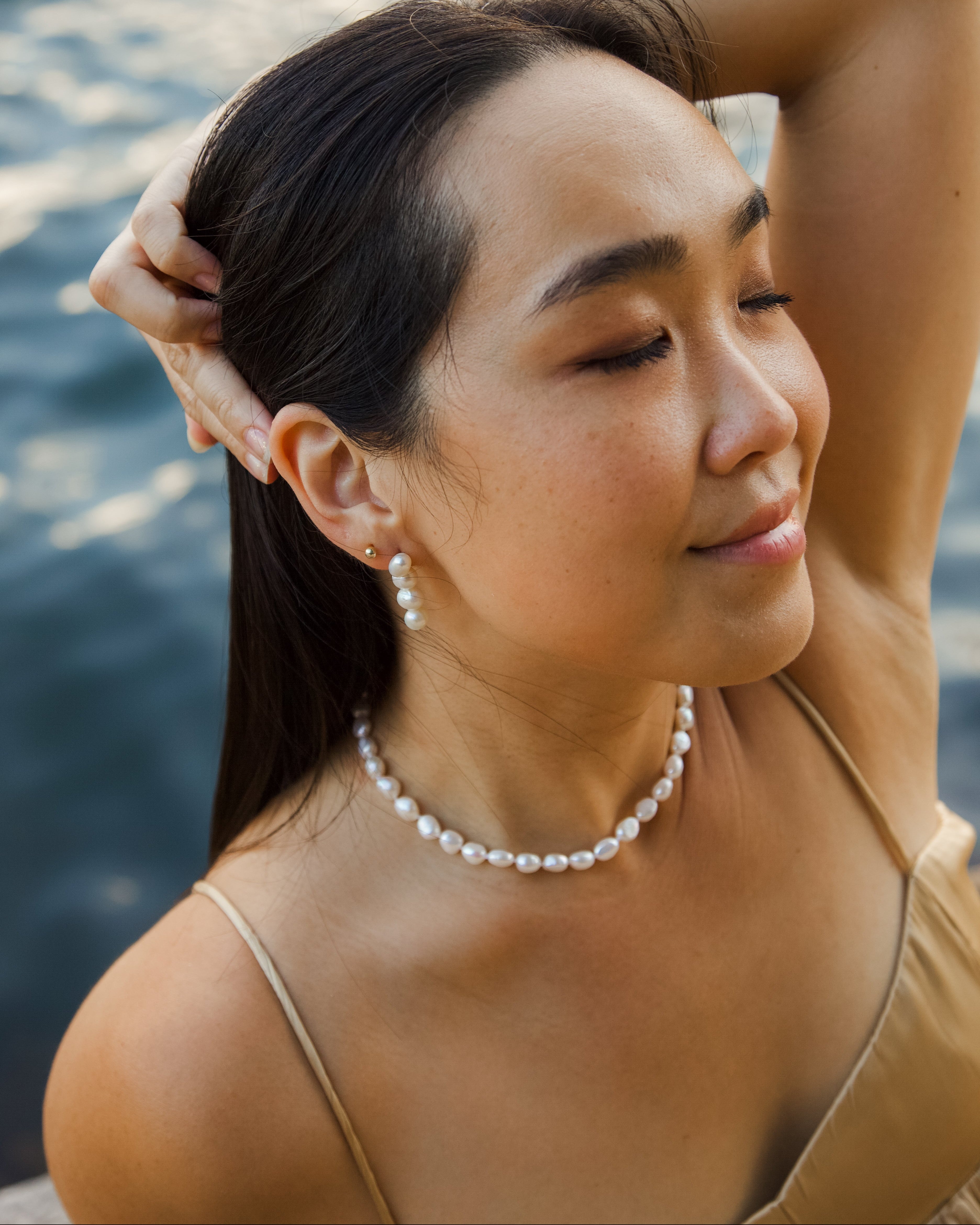 Woman with pearl necklace and earrings by water
