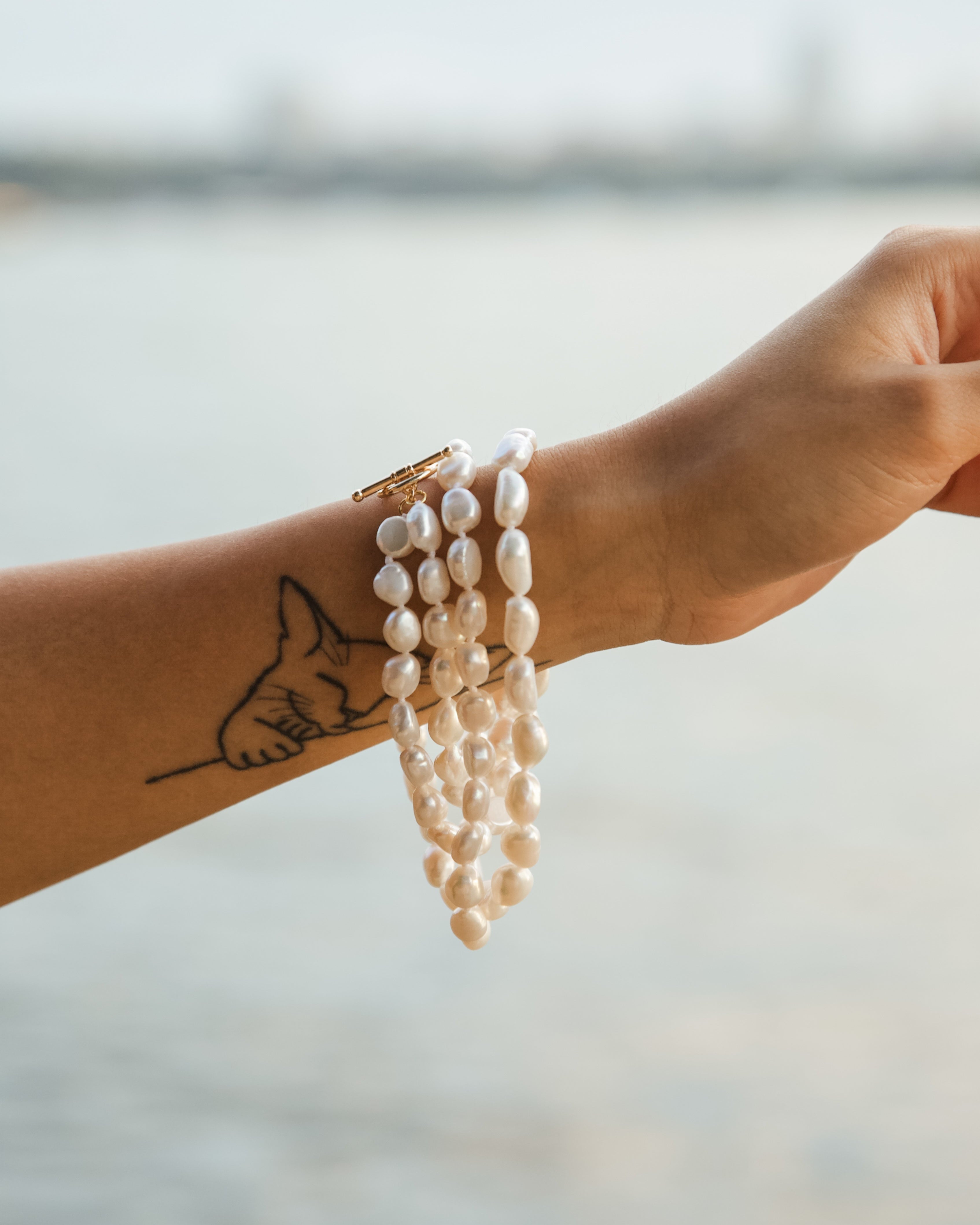 Hand wearing a pearl necklace wrapped around the wrist like a bracelet with a blurred natural background