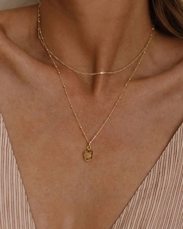 A person wearing a striped low-cut top and two layered necklaces, one choker with a small pendant and the other a longer chain.